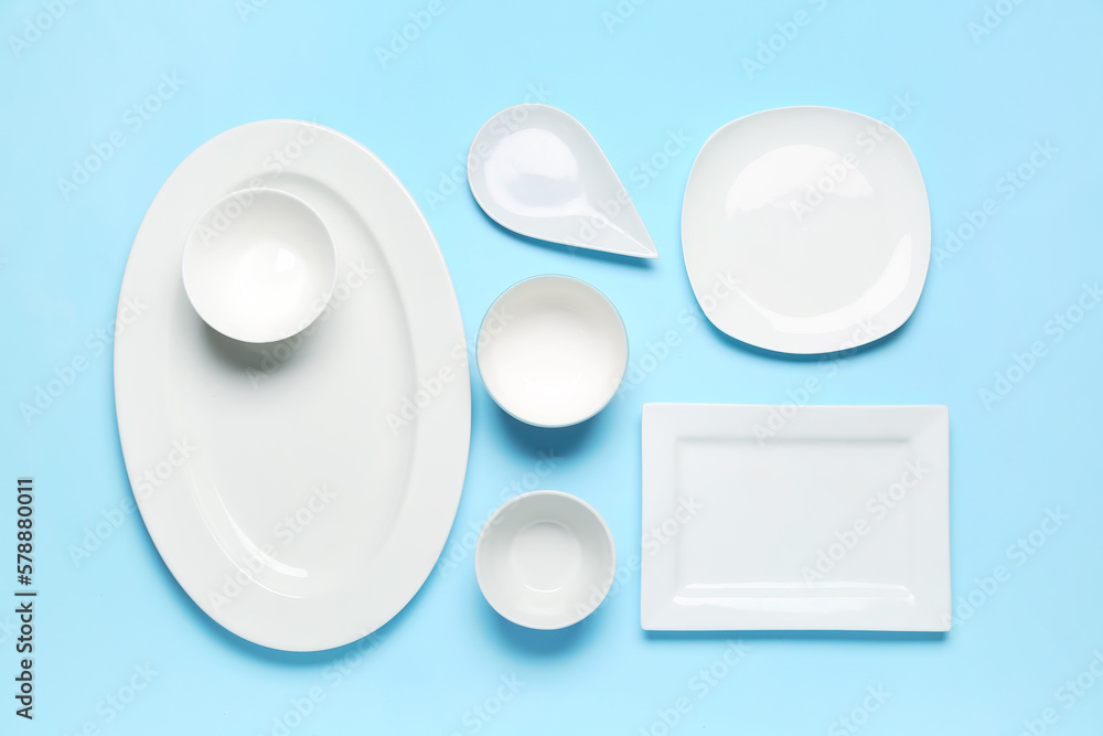 Composition with clean ceramic plates and bowls on blue background