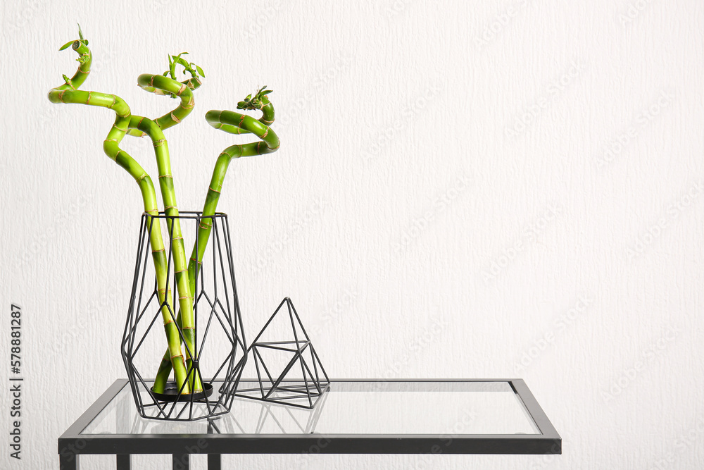 Vase with bamboo plant on table near white wall