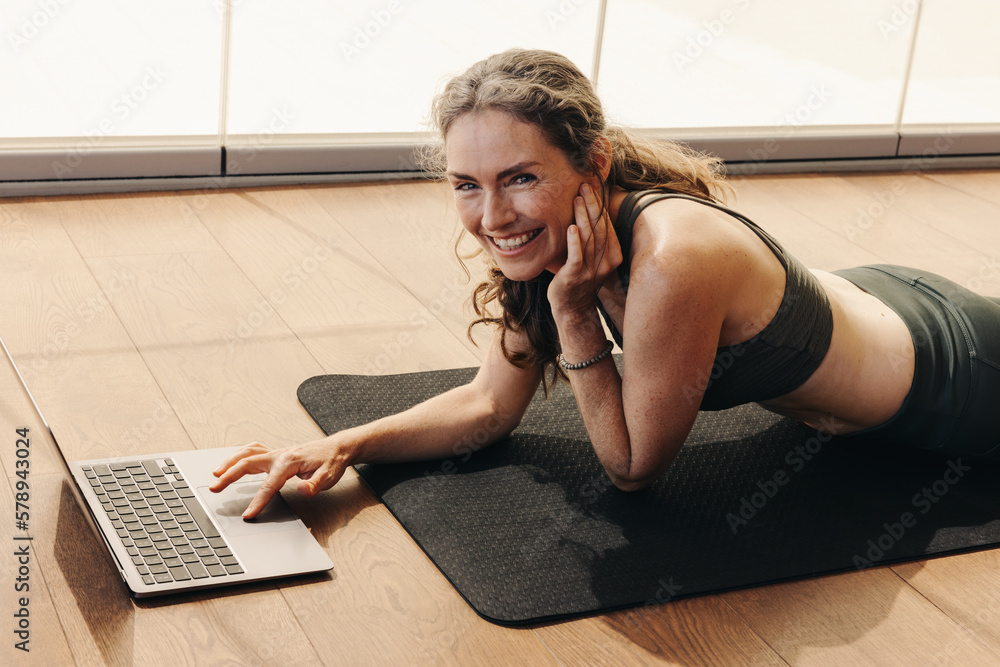 Mature woman smiling while joining an online yoga class on a laptop