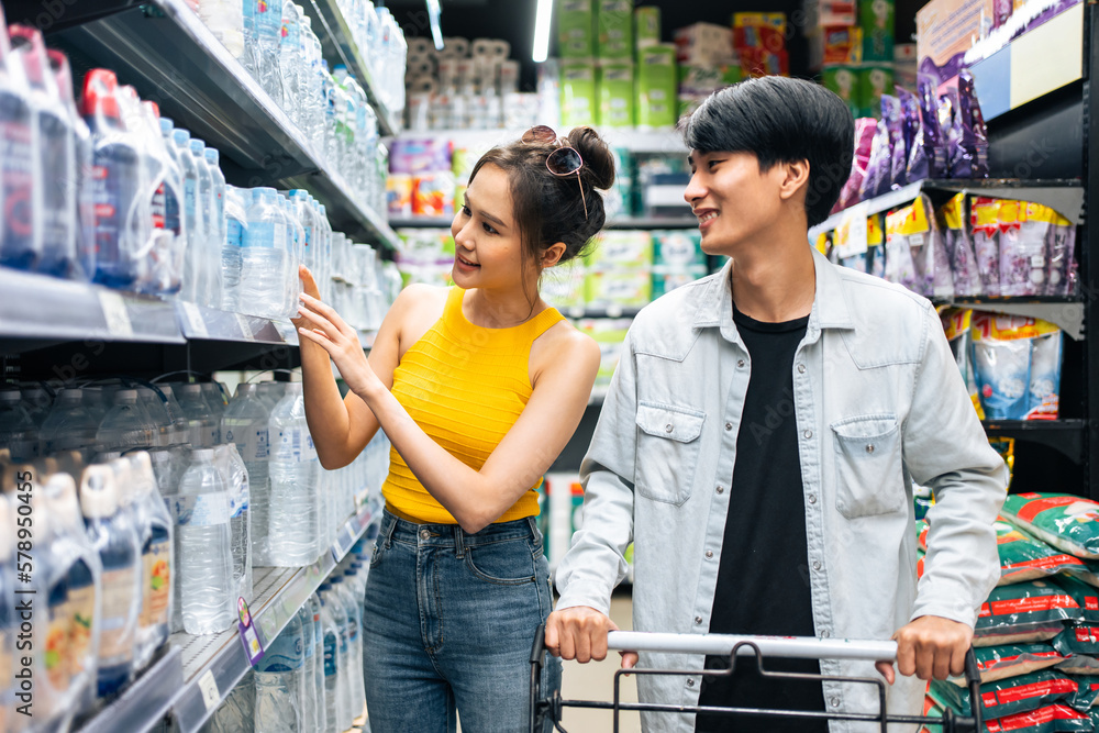 Asian young man and woman using cart to shoping goods in supermarket. 