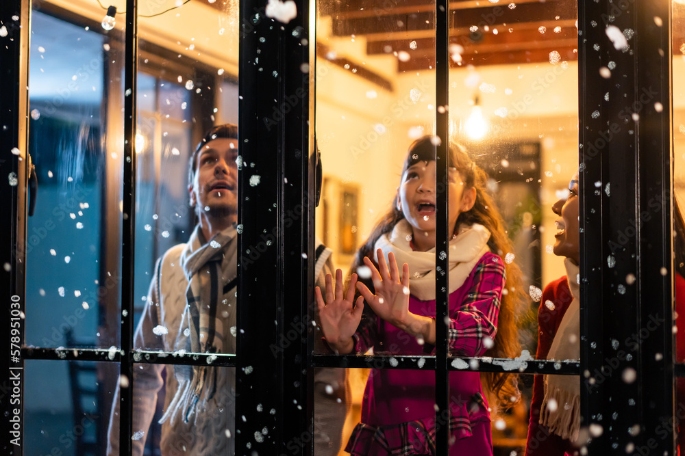 Adorable child looking at the window and first snow flakes with family. 