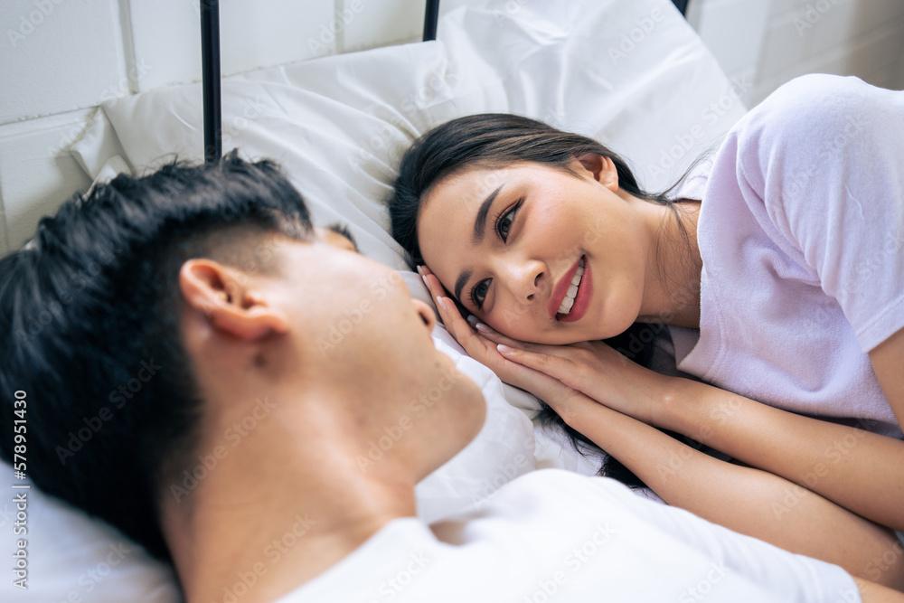 Asian new marriage couple lying down on bed and looking at each other. 