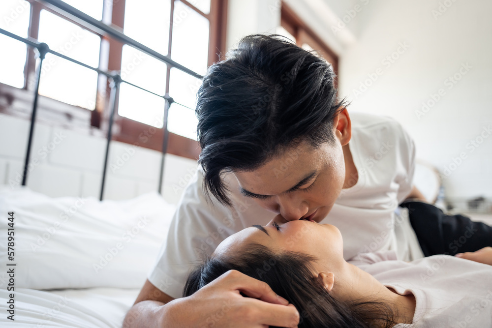 Asian husband kissing his wife while lying down sleep on bed in bedroom. 