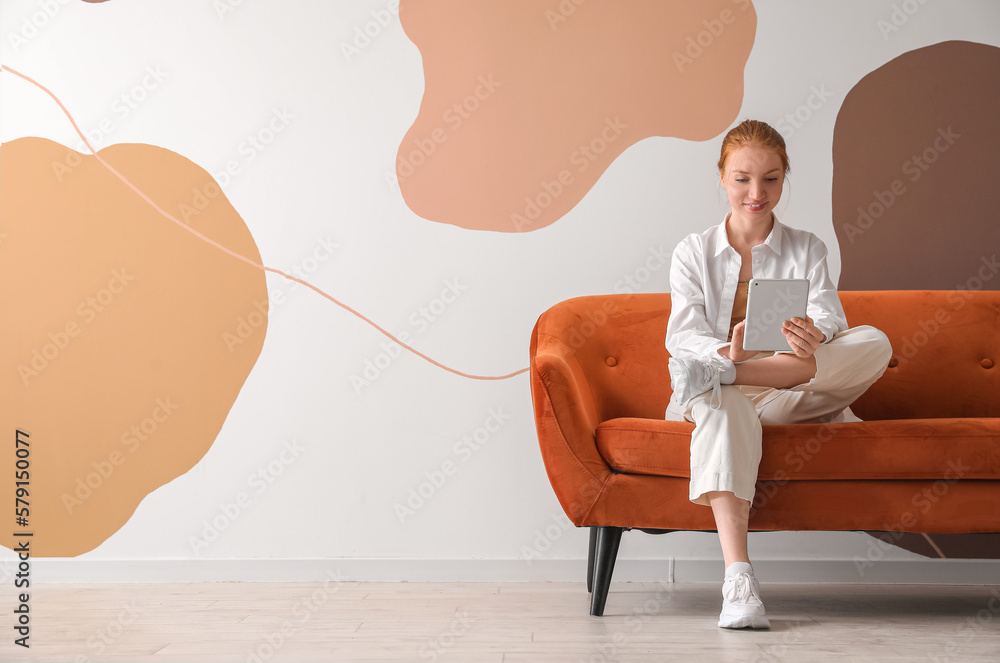 Beautiful woman using tablet computer on red sofa near color wall