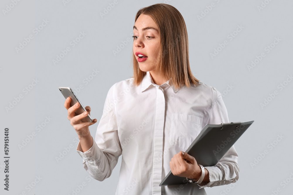 Female business consultant with clipboard using mobile phone on grey background