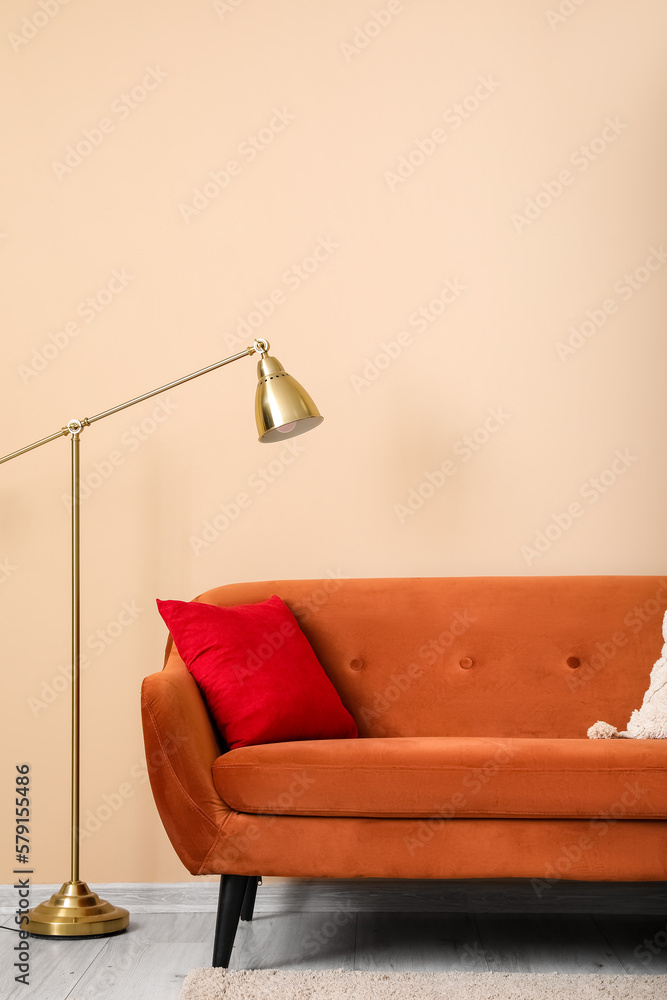 Brown sofa with cushion and lamp near beige wall