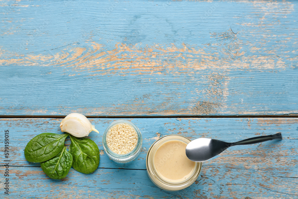 Jars with tasty tahini, sesame seeds, spinach and garlic on color wooden background