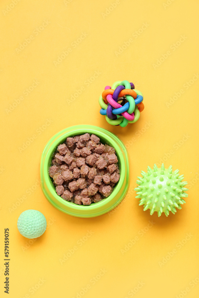 Bowl of wet pet food and balls on color background