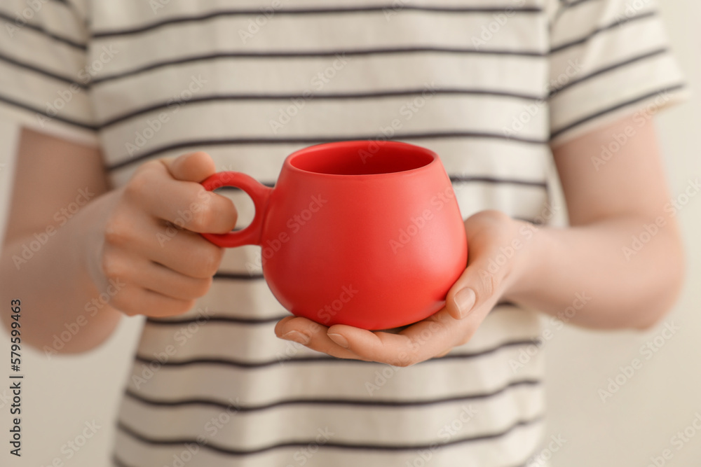 Woman holding red cup on beige background, closeup