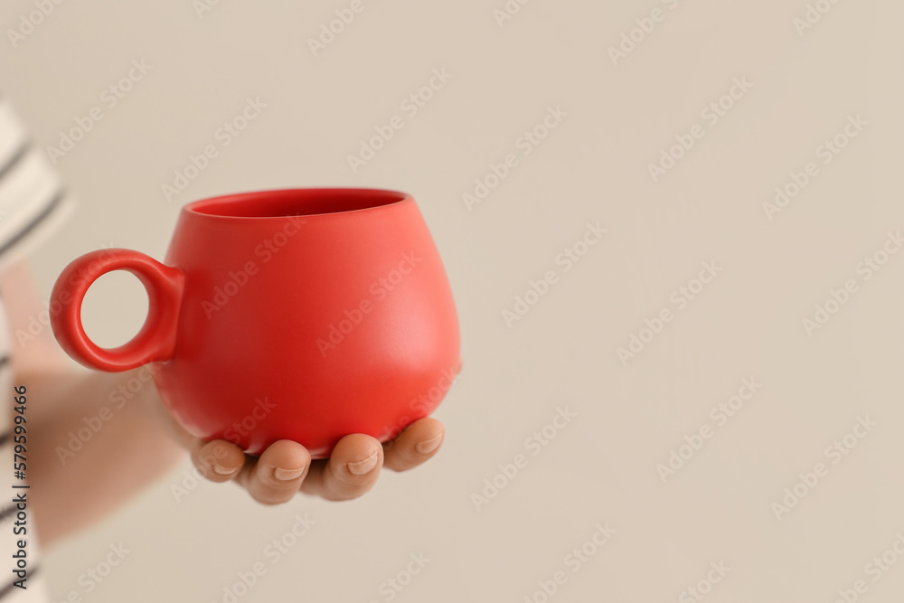 Woman holding red cup on beige background, closeup