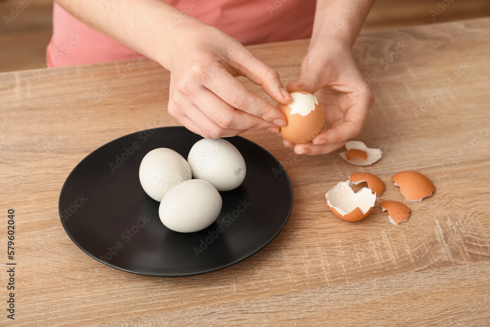 Woman peeling boiled egg at wooden table, closeup