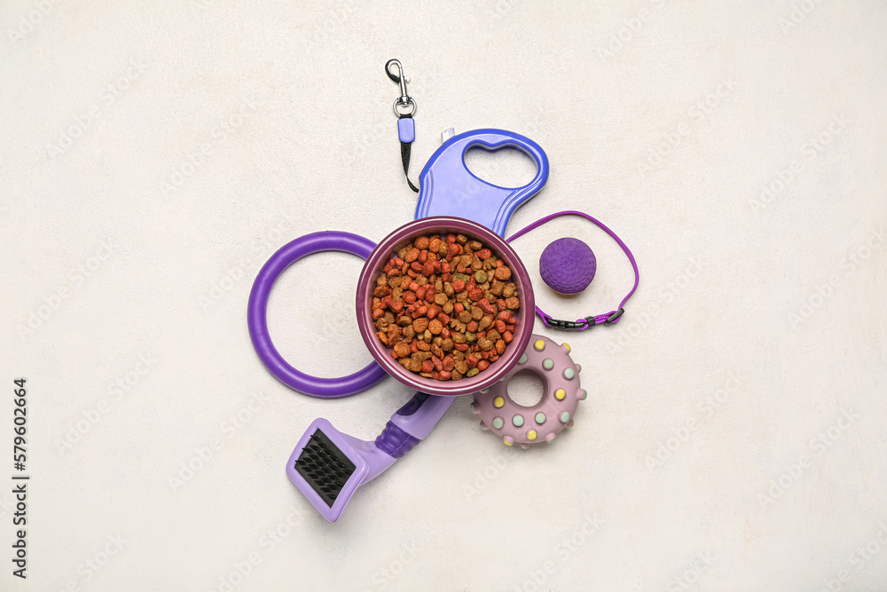 Bowl of dry pet food, toys and accessories on light background