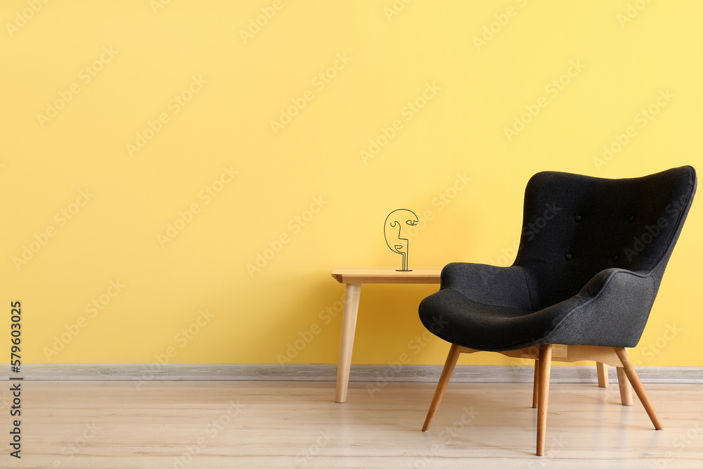 Stylish grey armchair and table near yellow wall