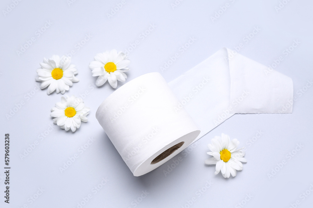 Roll of toilet paper and chamomile flowers on light background