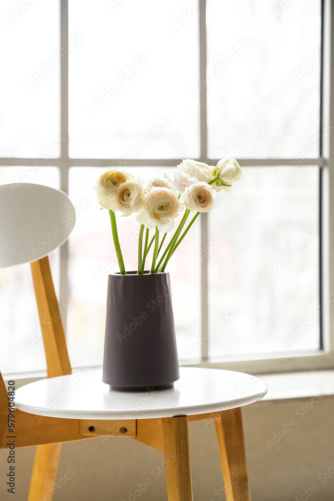 Vase with ranunculus flowers on chair near window in room, closeup