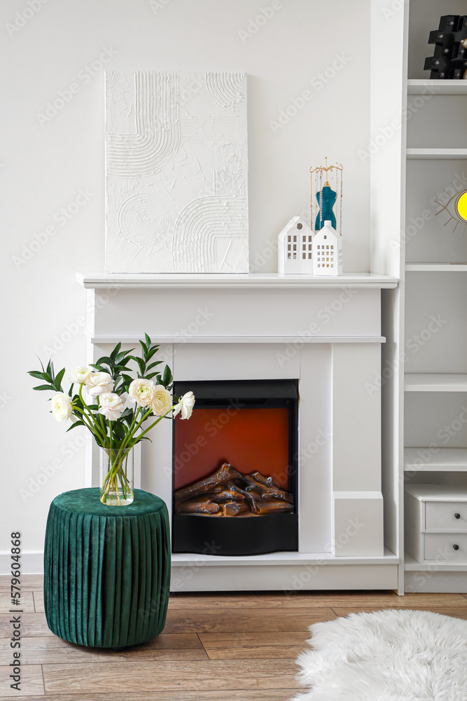 Vase with ranunculus flowers on pouf near fireplace in living room