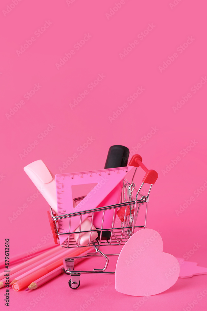 Shopping cart with different stationery on pink background