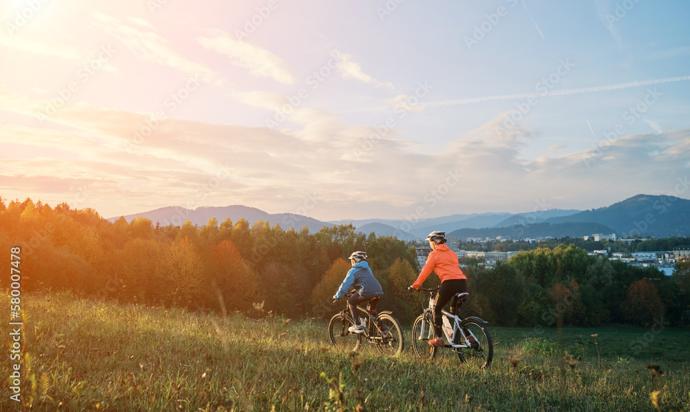 Mother and son ride a bike. Happy cute boy in helmet learn to riding a bike in park on green meadow 