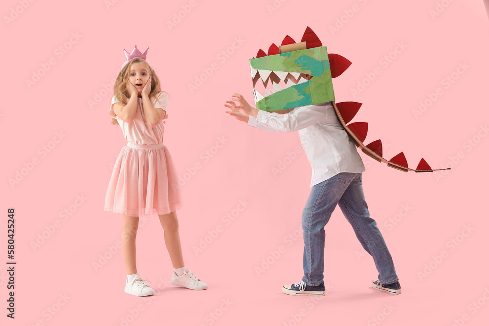 Scared little girl and her brother in cardboard dinosaur costume on pink background