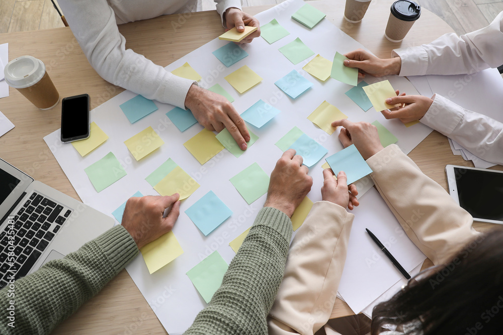 Group of people with sticky notes working on business plan at table in office, closeup