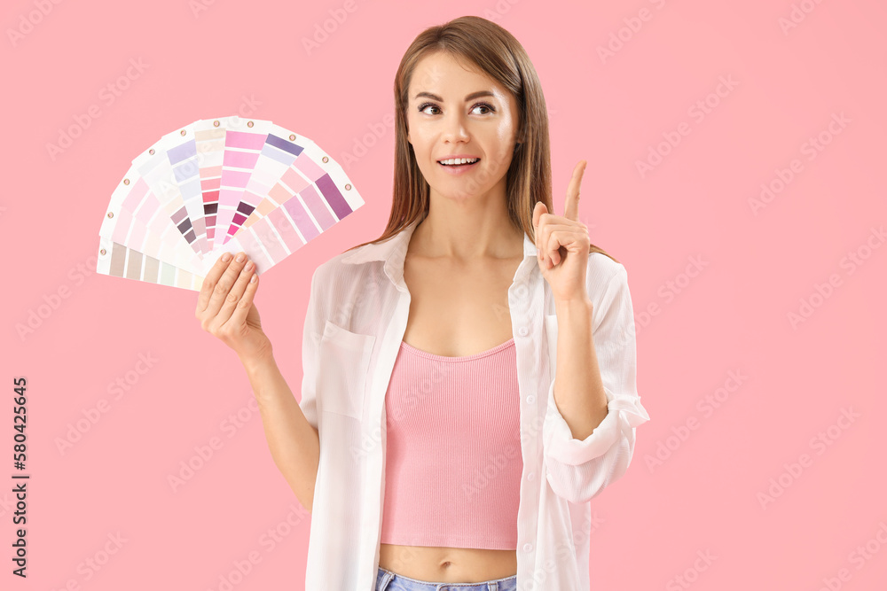 Beautiful woman with paint color palettes pointing at something on pink background