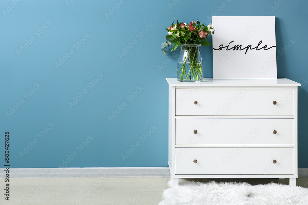 Vase with beautiful alstroemeria flowers on drawer and poster with word SIMPLE near blue wall