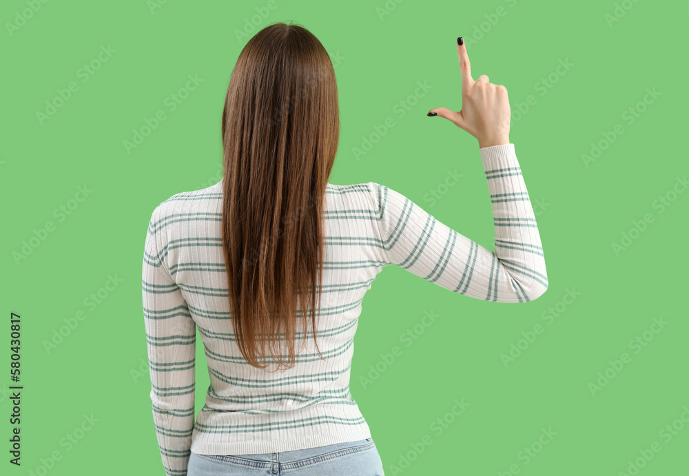 Young woman showing loser gesture on green background, back view