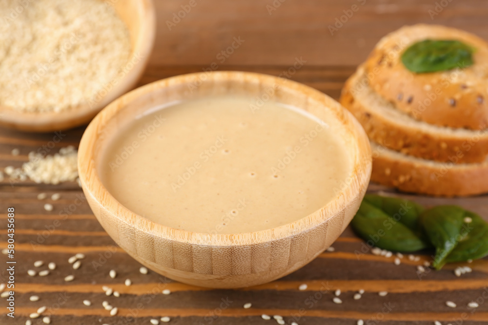 Bowl of tasty tahini, spinach and bread on wooden table, closeup