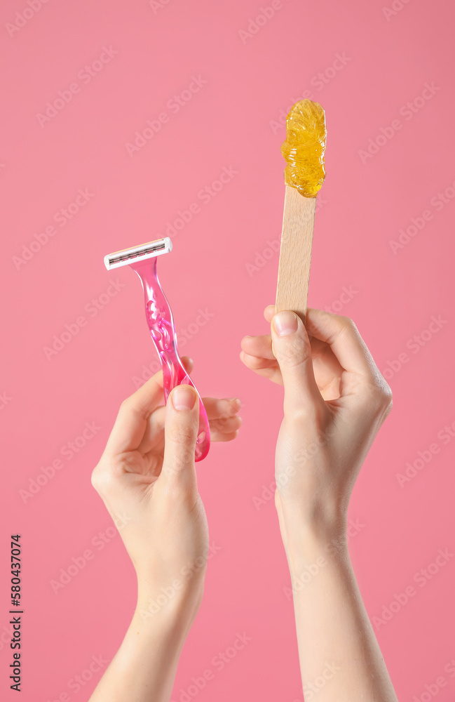 Hands holding spatula with sugaring paste and razor on pink background. Hair removal concept