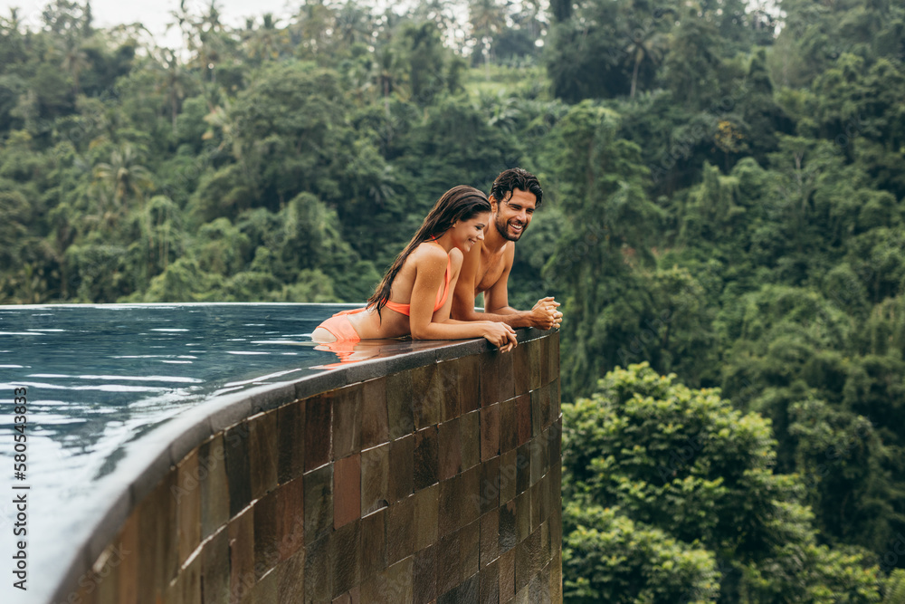 Happy young couple standing at edge of swimming pool