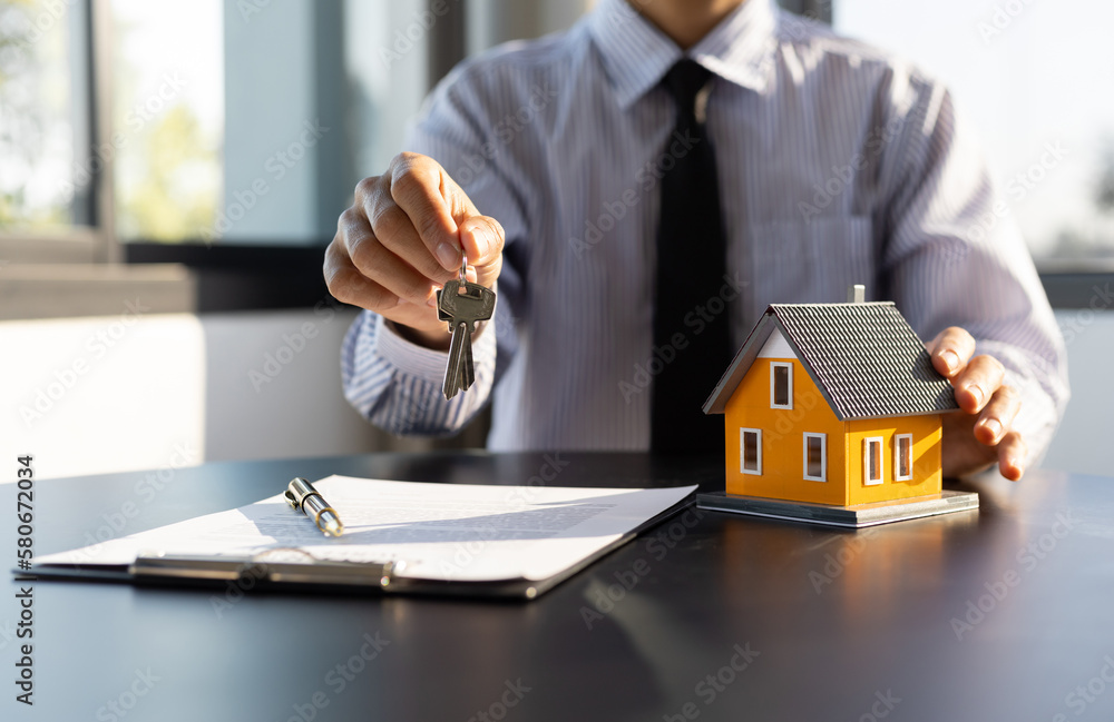 Real estate agent holding keys and model house showing to client, rental house concept.