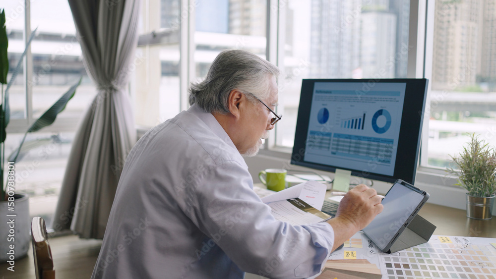 Asian senior mature man working with computers and tablet on table desk at home