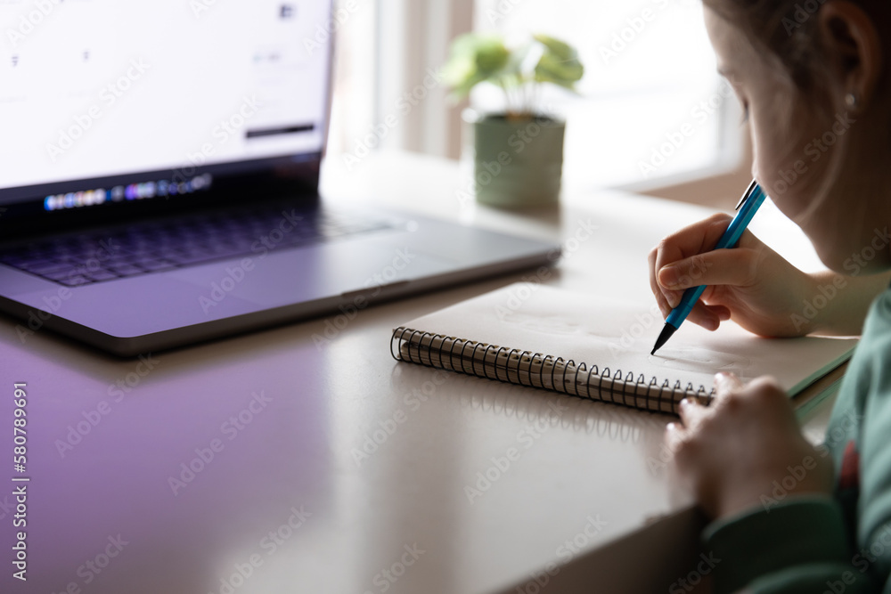 A little girl writes with a pen in a notebook, does her homework.