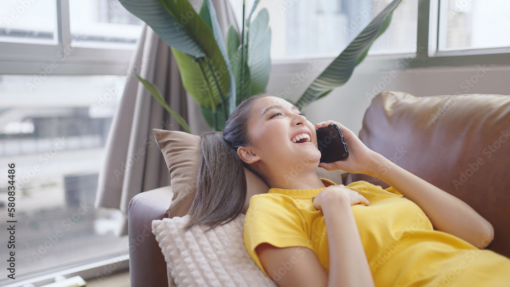 Young Asian woman using smartphone lay on sofa happy and smile.