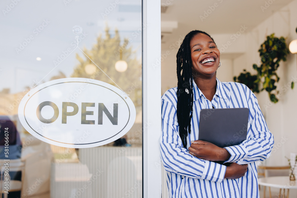 Cheerful young restaurant owner standing next to an open sign at the doorway of her new cafe