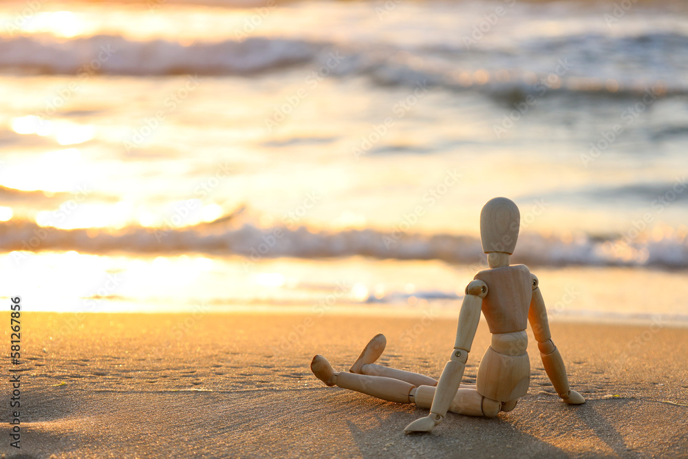 Wooden mannequin on sand near sea at sunset