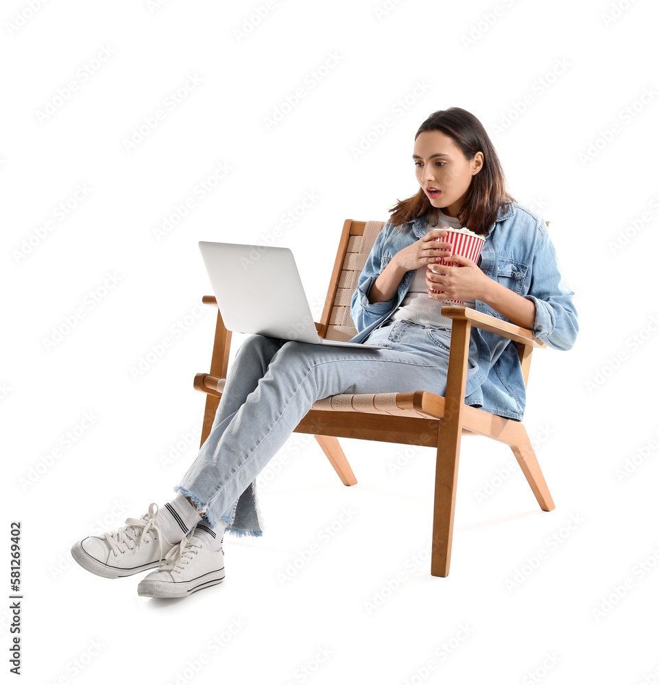 Shocked young woman with popcorn and laptop watching video in armchair on white background