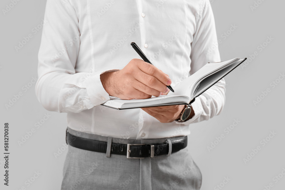 Business consultant writing in notebook on grey background, closeup