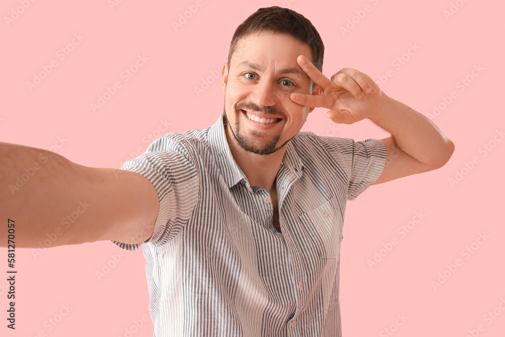 Handsome man in shirt showing victory gesture on pink background, closeup