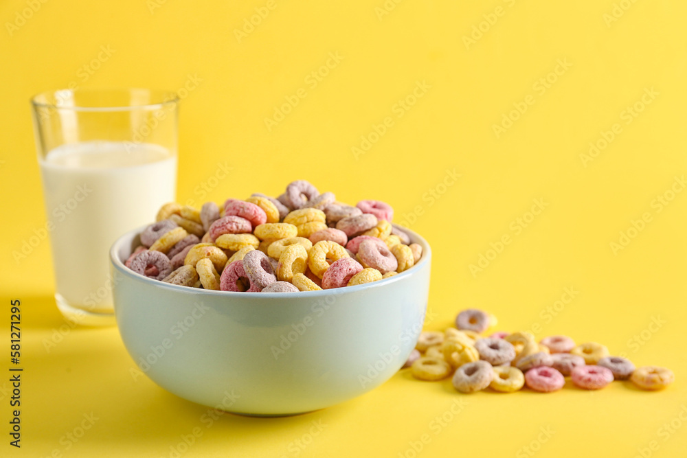 Bowl of colorful cereal rings and glass of milk on yellow background