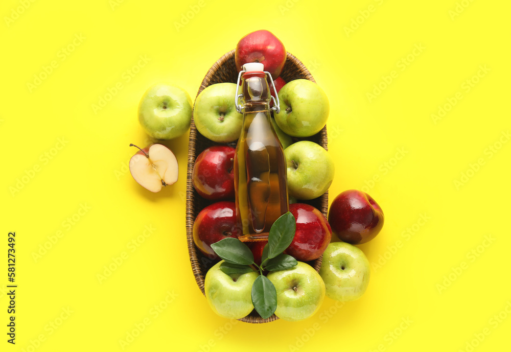 Basket with glass bottle of fresh apple cider vinegar and fruits on yellow background