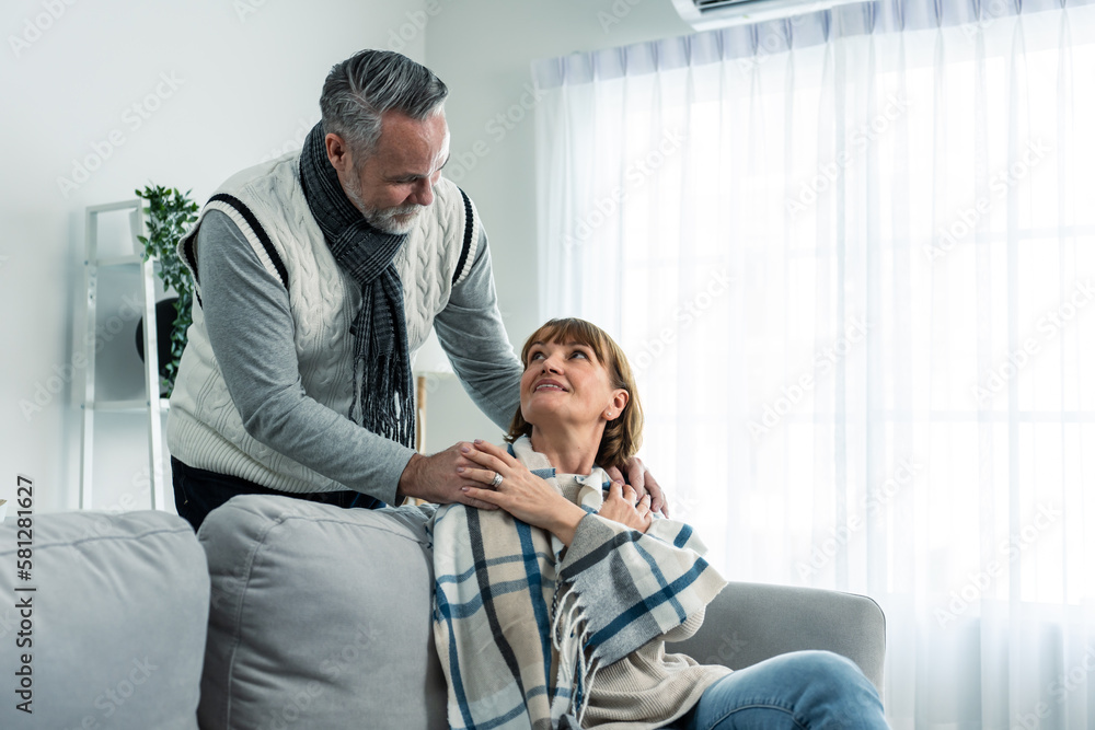 Caucasian senior man taking care of elderly sick wife in living room.