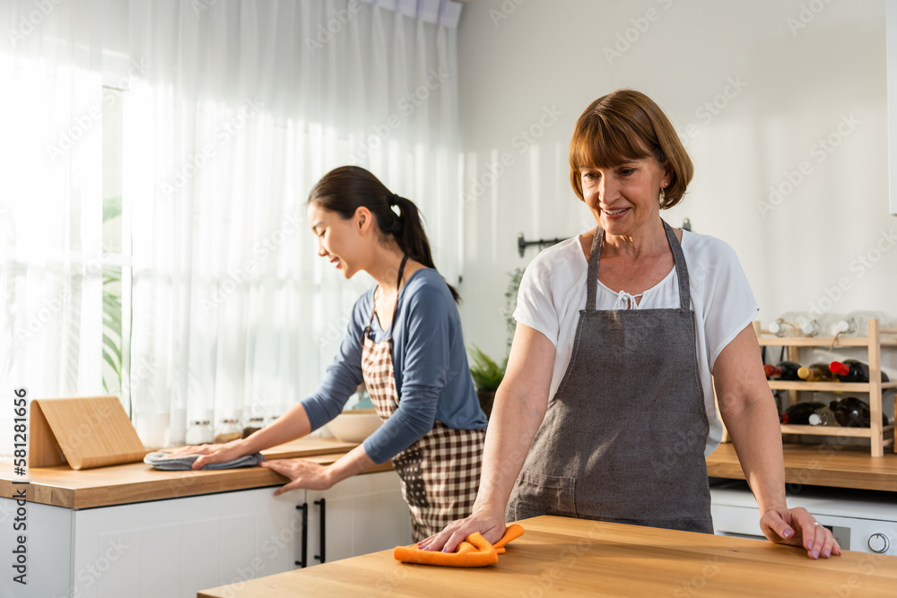 Caucasian senior elderly woman cleaning kitchen in house with daughter. 