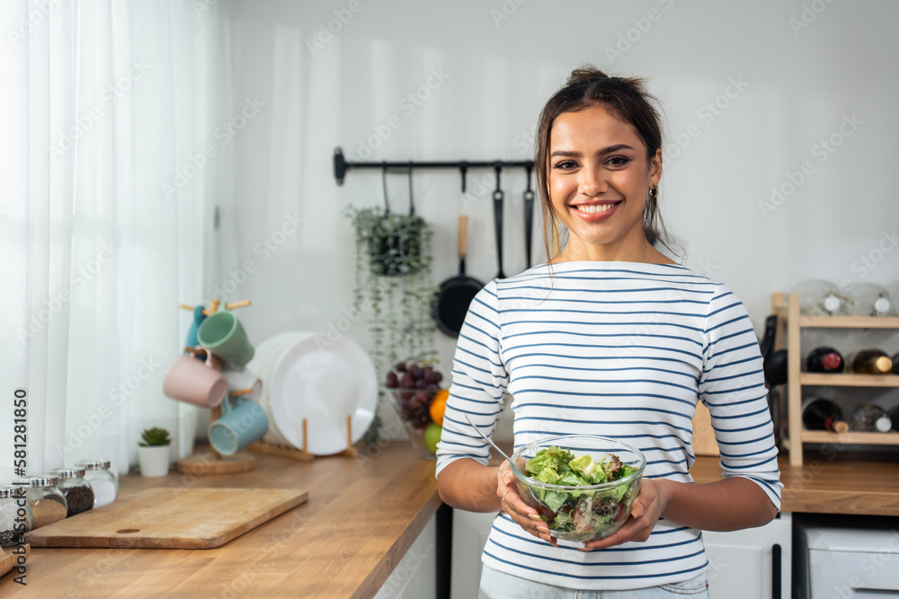 Portrait of young Caucasian girl eating green salad in kitchen at home.