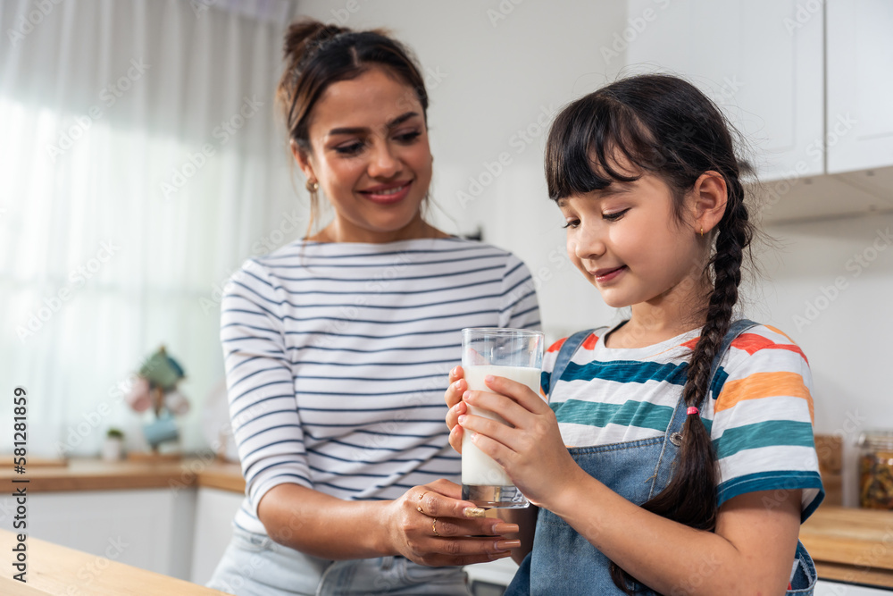 Caucasian little kid holding a cup of milk and drinking with mother. 