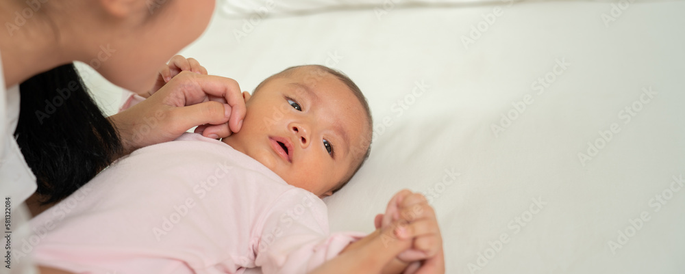 Loving Asian Mom carying of her newborn baby at home in the bedroom. happy family. mother playing wi