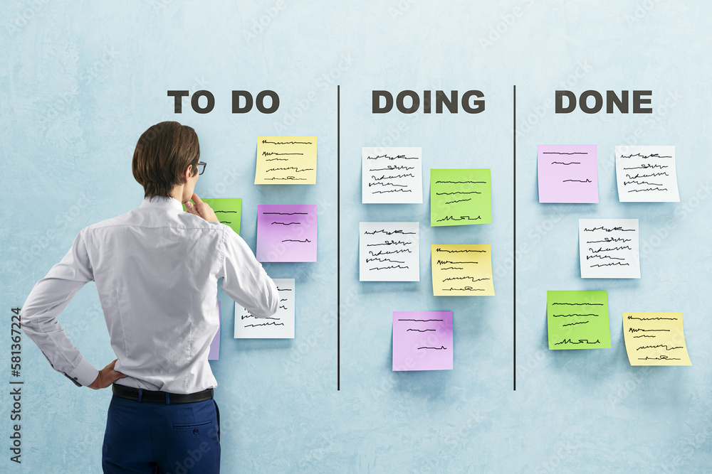 Back view of young european businessman with creative to do lists, glued paper stickers on blue wall