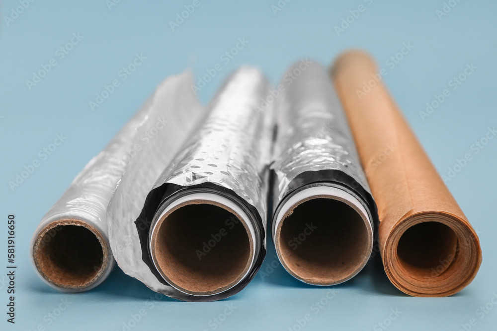 Rolls of aluminium foil, baking paper and food film on color background, closeup