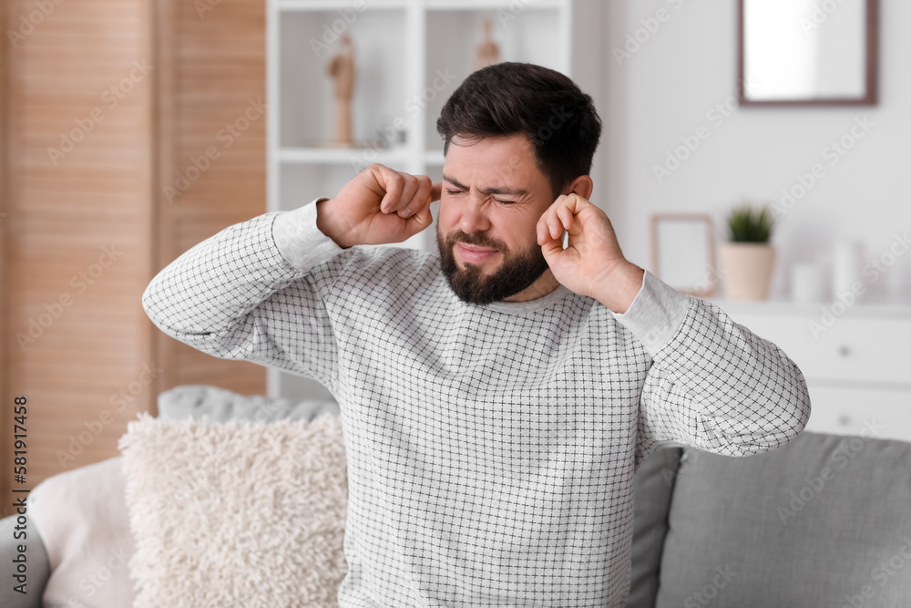 Angry young man suffering from loud noise at home