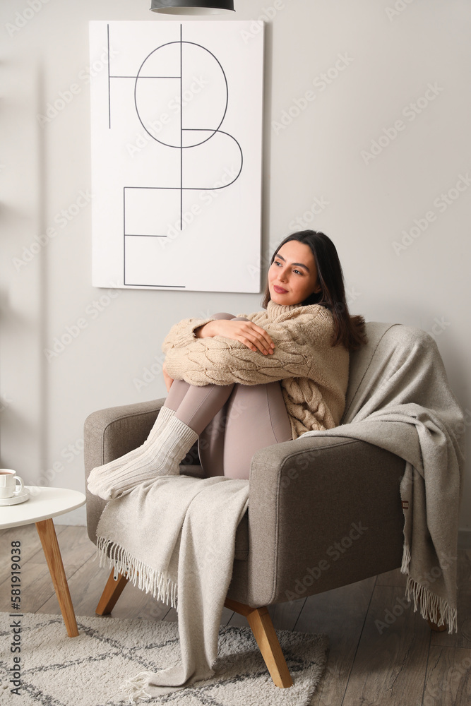 Young woman sitting in soft armchair at home